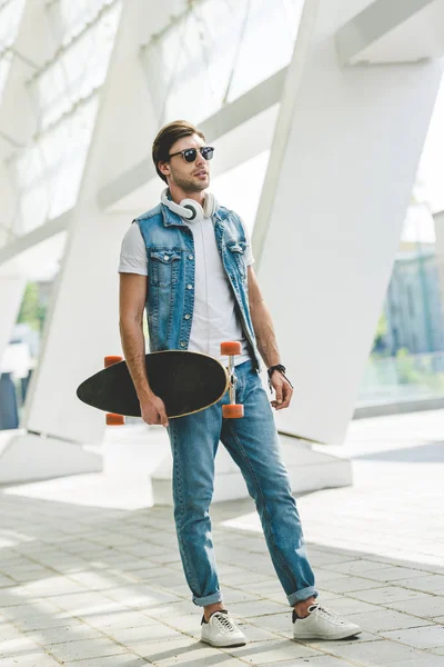 Skateboarder Muda Dalam Pakaian Denim Dengan Longboard Dan Headphone — Foto Stok Gratis