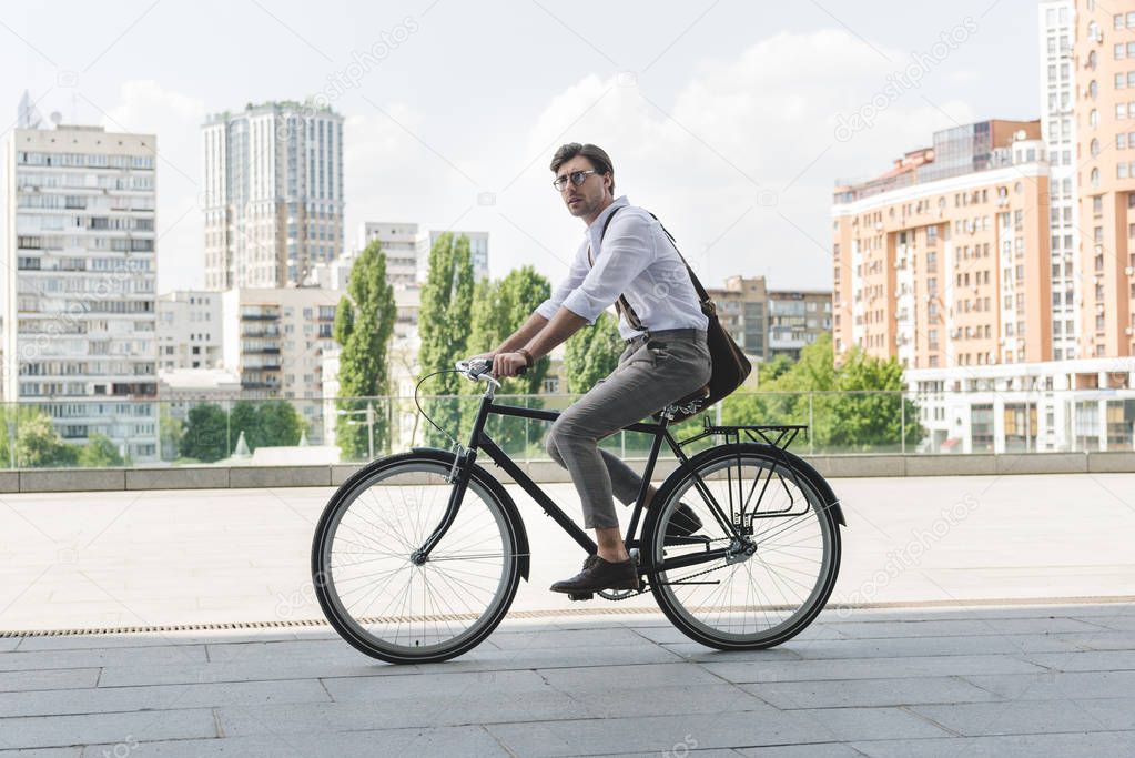 side view of attractive young man in stylish clothes riding vintage bicycle on city street