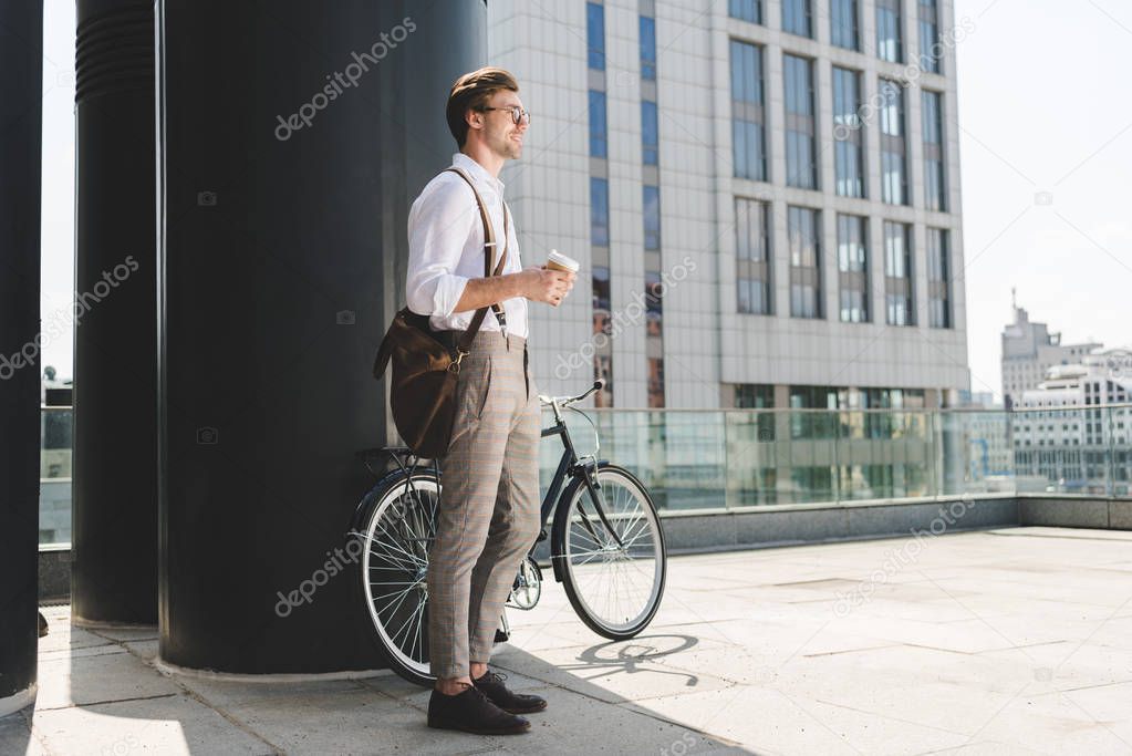 smiling young man with coffee to go and vintage bicycle on rooftop of business building