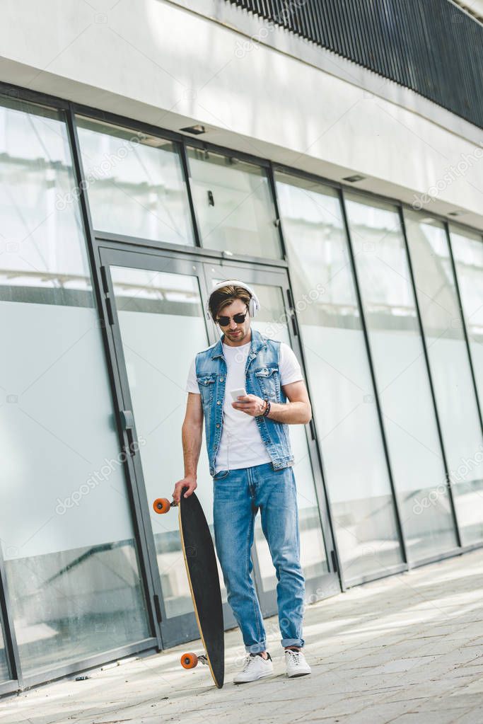 handsome young skateboarder with longboard using smartphone