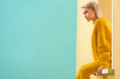 Seitenansicht einer stilvollen Frau in gelbem Pullover und Strumpfhose, die am dekorativen Fenster sitzt