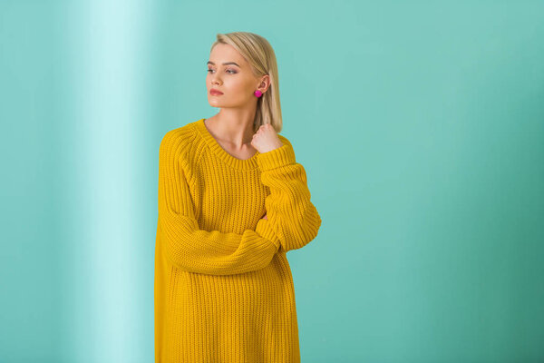 портрет красивой задумчивой женщины в желтом свитере, позирующей на синем фоне
