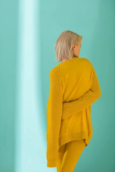 蓝色背景下穿黄色毛衣的女人的背影 — 免费的图库照片