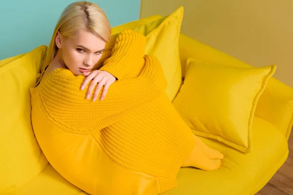 黄色的沙发上穿黄毛衣和紧身衣的年轻沉思妇女的侧面视图 — 图库照片