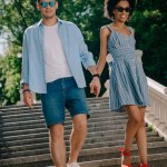 Stilvolles junges Paar mit Sonnenbrille hält Händchen und geht im Park die Treppe hinunter