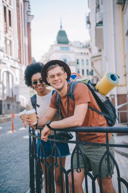 happy young interracial couple of travelers with paper cups of coffee clipart