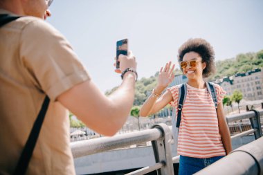 erkek Gezgin kız sallanan el smartphone cep telefonu ile gülümseyen fotoğrafını resmini kırpılmış 