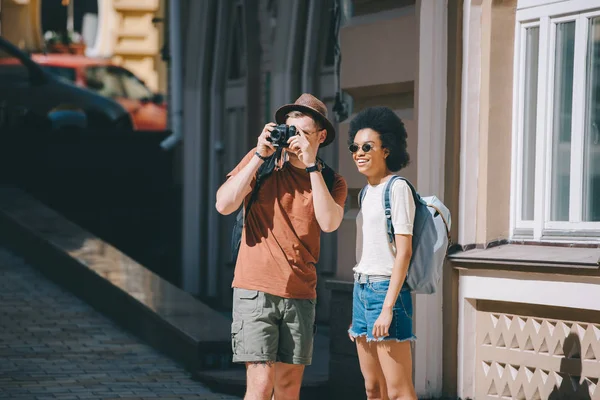 カメラとアフリカ系アメリカ人のガール フレンドの近くに立って写真を撮る男性旅行者 — ストック写真