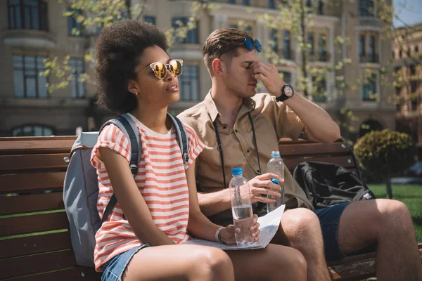 Pareja Interracial Cansado Viajeros Con Botellas Agua Mapa Sentado Banco — Foto de stock gratuita