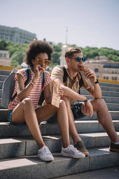 Multiethnic Couple Travelers Sitting Stairs Eating Croissants — Stock Photo, Image