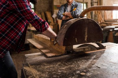 marangoz Kareli gömlekli makine testere ve kereste fabrikası arkasında duran ortağı kullanarak kırpılmış atış