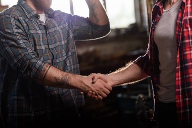 cropped shot of carpenter with tattooed hand shaking hand of partner at sawmill  clipart