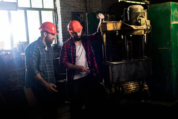carpenters in protective helmets using machine tool at sawmill 