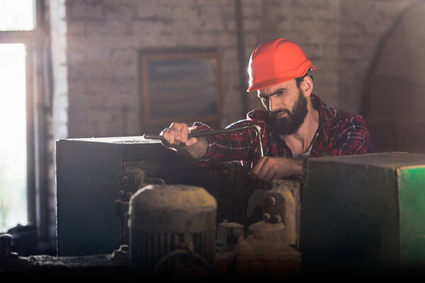 serious worker in protective helmet repairing machine tool at sawmill 