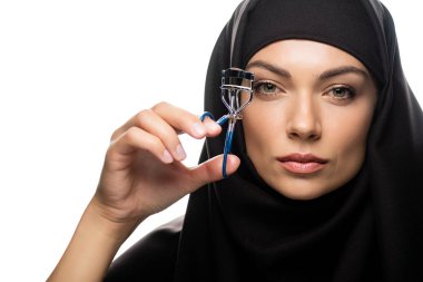 Kirpik bigudi kullanan tesettürlü genç Müslüman kadın beyaza izole edilmiş.