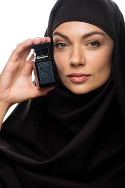 tesettürlü genç Müslüman kadın beyaz bir parfüm şişesi tutuyor.