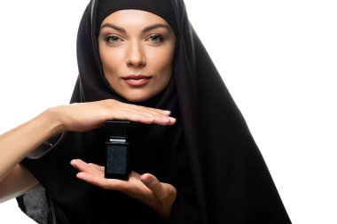 tesettürlü genç Müslüman kadın beyaz bir parfüm şişesi tutuyor.