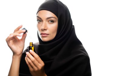 tesettürlü genç Müslüman bir kadın elinde damlatıcıyla beyaz serumla bir şişe tutuyor.