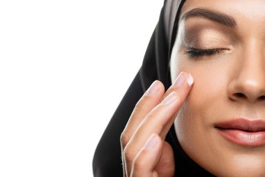 Genç Müslüman kadın tesettürlü yüz kremi sürüyor. Gözleri kapalı ve beyaz tenli.
