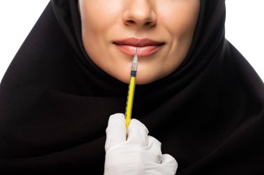 partial view of young Muslim woman in hijab having beauty injection isolated on white, lip augmentation concept clipart