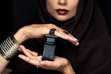 Altın takılarla süslenmiş tesettürlü güzel bir Müslüman kadın. Siyah üzerine izole edilmiş parfüm taşıyor.