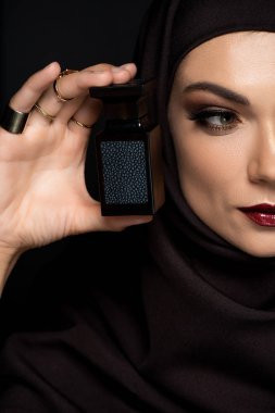 Altın takılarla süslenmiş tesettürlü güzel bir Müslüman kadın. Siyah üzerine izole edilmiş parfüm taşıyor.