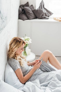 Mutlu kız, evinde çiçeklerle birlikte komodinin yanında akıllı telefon kullanıyor. 