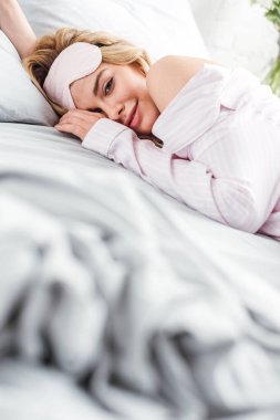 Gözlerinde maske olan neşeli bir kadının seçici odağı evde yatakta yatıyor. 