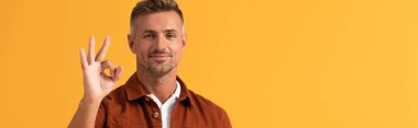 Neşeli adamın turuncu üzerine izole edilmiş tamam işareti gösteren panoramik çekimi. 