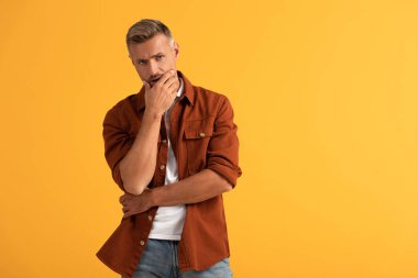 Düşünceli adam yüzüne dokunuyor ve turuncu üzerine izole edilmiş kameraya bakıyor. 