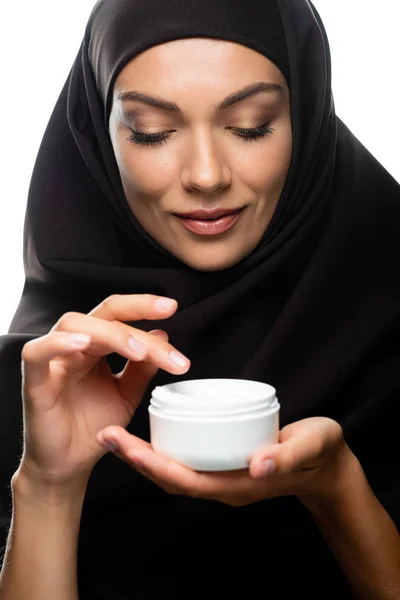 头戴头巾的年轻穆斯林妇女拿着装有用白色隔开的化妆品霜的容器 — 图库照片