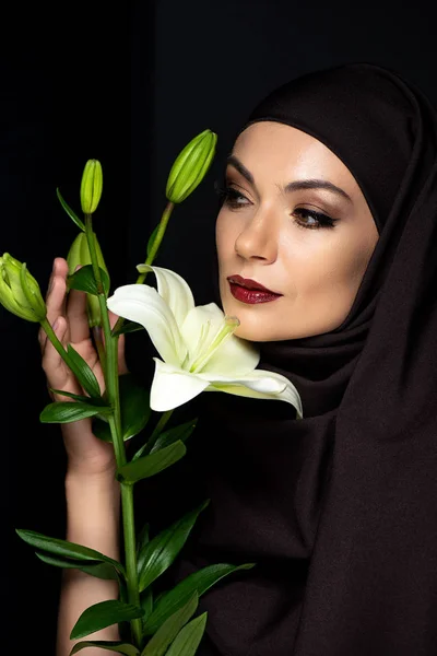 有魅力的穆斯林女子 头戴头巾 红唇紧握百合花 与黑色隔离 — 图库照片