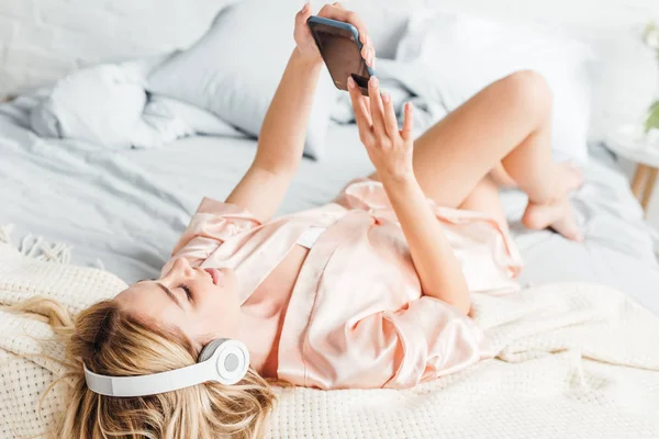 Selektywne Skupienie Szczęśliwej Dziewczynie Korzystającej Smartfona Słuchającej Muzyki Leżącej Łóżku — Zdjęcie stockowe