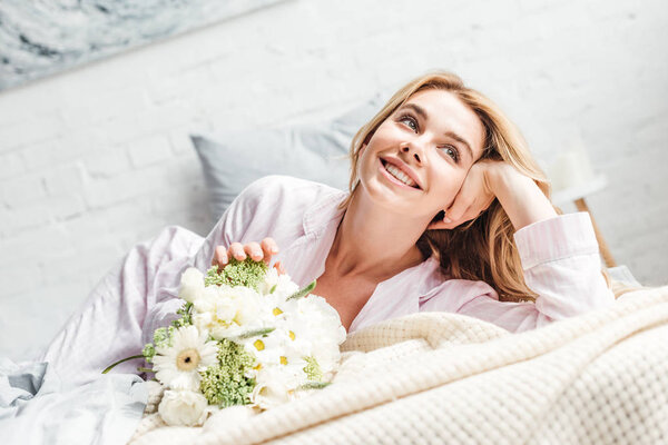 селективное внимание веселой молодой женщины, лежащей рядом с цветами на кровати
 