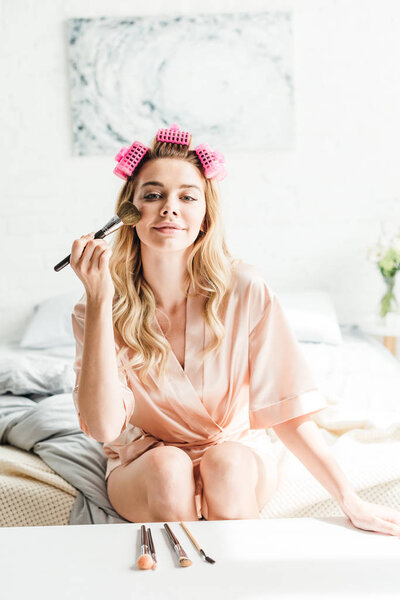 happy girl in hair curlers holding cosmetic brush near face 