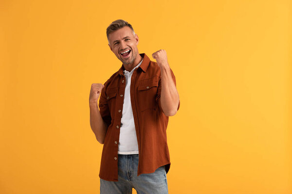 excited man with clenched fists isolated on orange 
