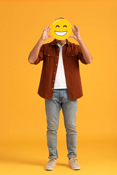 KYIV, UKRAINE - SEPTEMBER 24, 2019: man covering face with happy emoticon on orange 