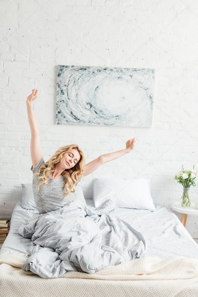 happy young woman sitting with outstretched hands while waking up at home 