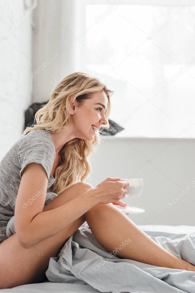 side view of happy woman holding cup of coffee in bed 