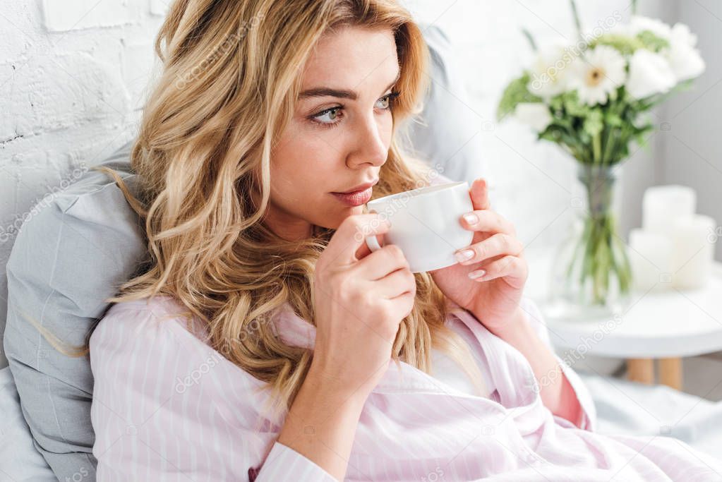 attractive woman holding cup with coffee in bed 