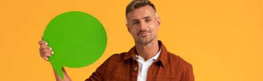 Turuncu üzerinde yeşil konuşma balonu tutan mutlu adamın panoramik görüntüsü. 