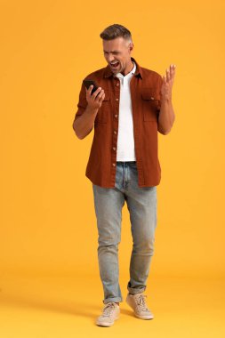 Kızgın adam turuncu üzerine akıllı telefon tutarken çığlık atıyor. 