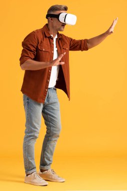 handsome man in virtual reality headset gesturing while standing on orange 
