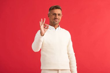 Gözlüklü mutlu adam kırmızıda izole edilmiş tamam işareti gösteriyor. 