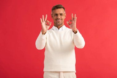 Gözlüklü neşeli adam kırmızıda izole edilmiş tamam işareti gösteriyor. 