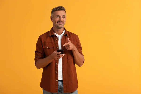 Homme Heureux Pointant Doigt Smartphone Isolé Sur Orange — Photo