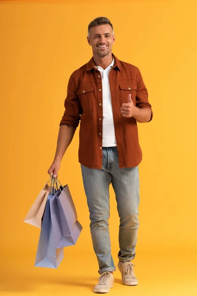 Vrolijk Man Met Kleurrijke Boodschappentassen Duim Omhoog Oranje — Stockfoto