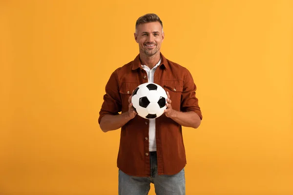 cheerful man holding football isolated on orange 
