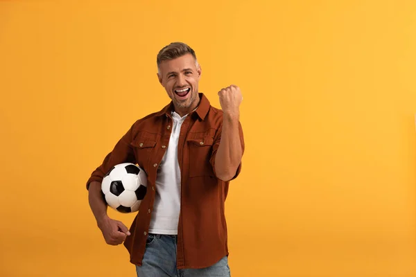 happy man standing with football and celebrating isolated on orange 