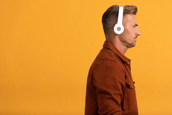 在用橙色隔离的无线耳机听音乐的英俊男人的侧视图 — 图库照片